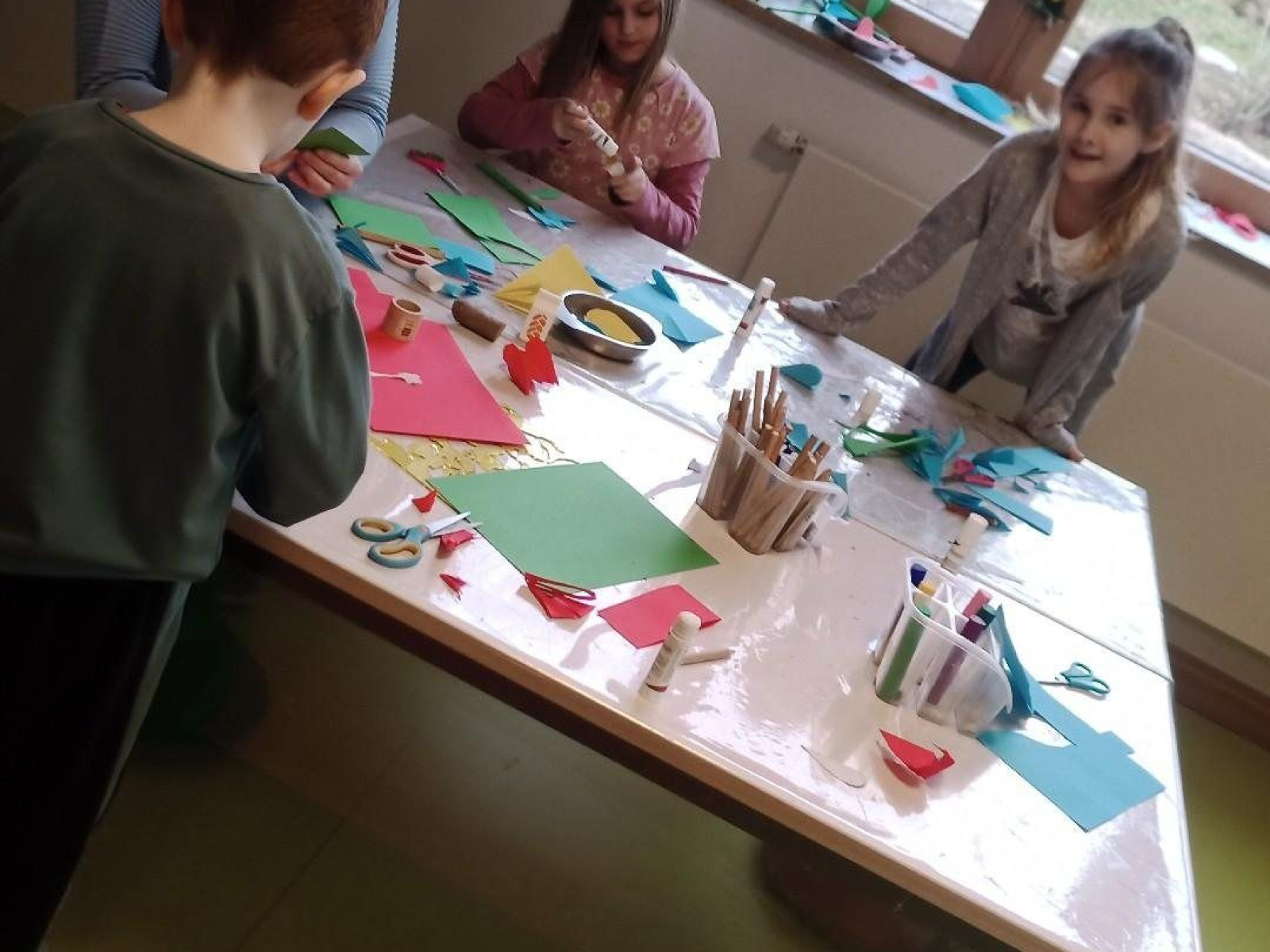 Kinder beim Basteln mit Papier an einem Tisch in einem hellen Raum.