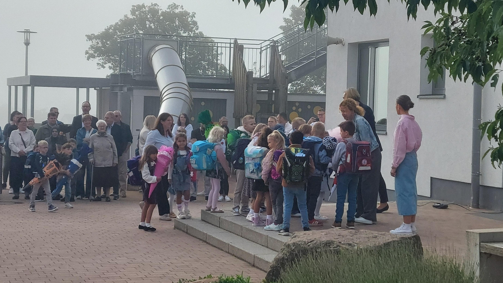 Kinder und Eltern versammeln sich vor einem Schulgebäude am ersten Schultag.