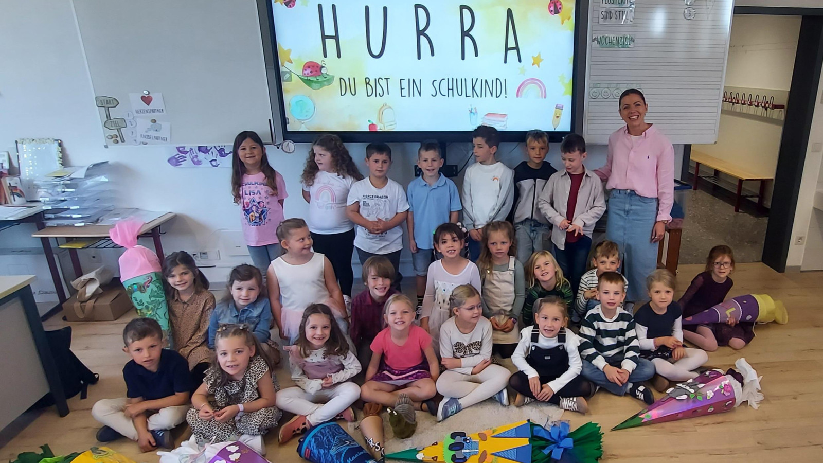 Eine Gruppe von Kindern und eine Lehrerin im Klassenzimmer, jedes Kind hält eine Schultüte.