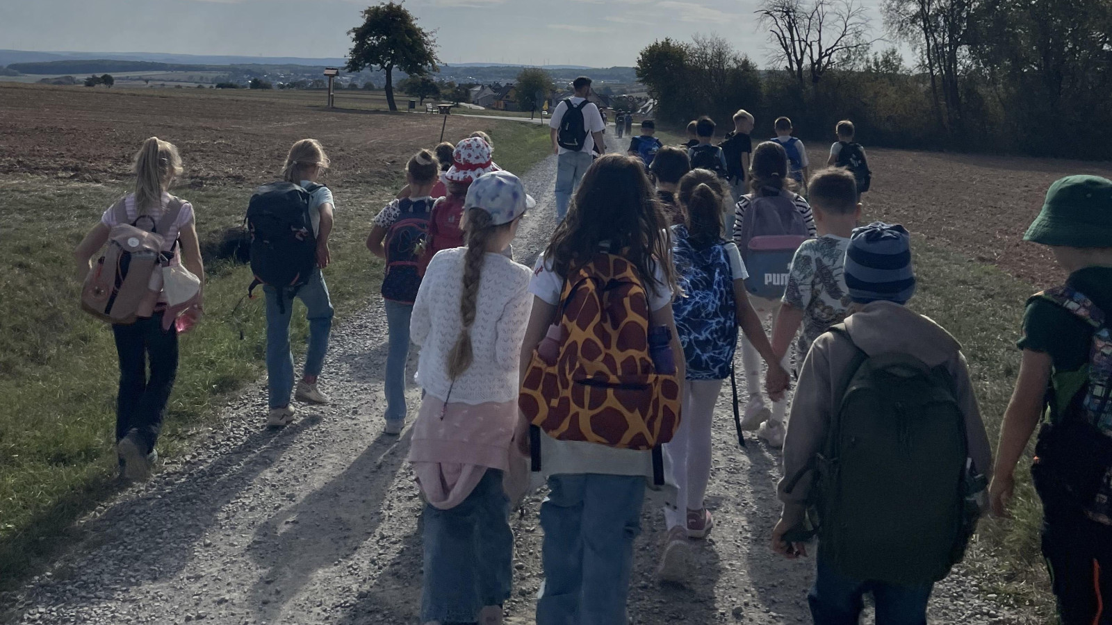 Kinder gehen auf einem ländlichen Weg, sonniges Wetter und blauer Himmel im Hintergrund.