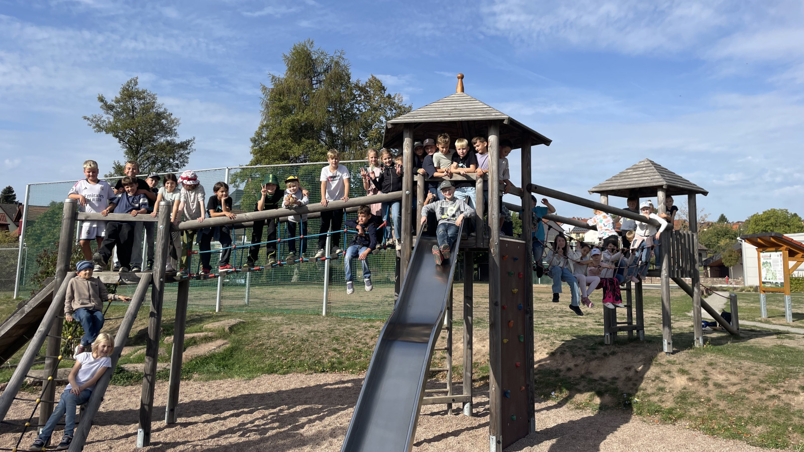 Menschen auf einem Spielplatz mit Klettergerüst und Rutsche. Blauer Himmel im Hintergrund.