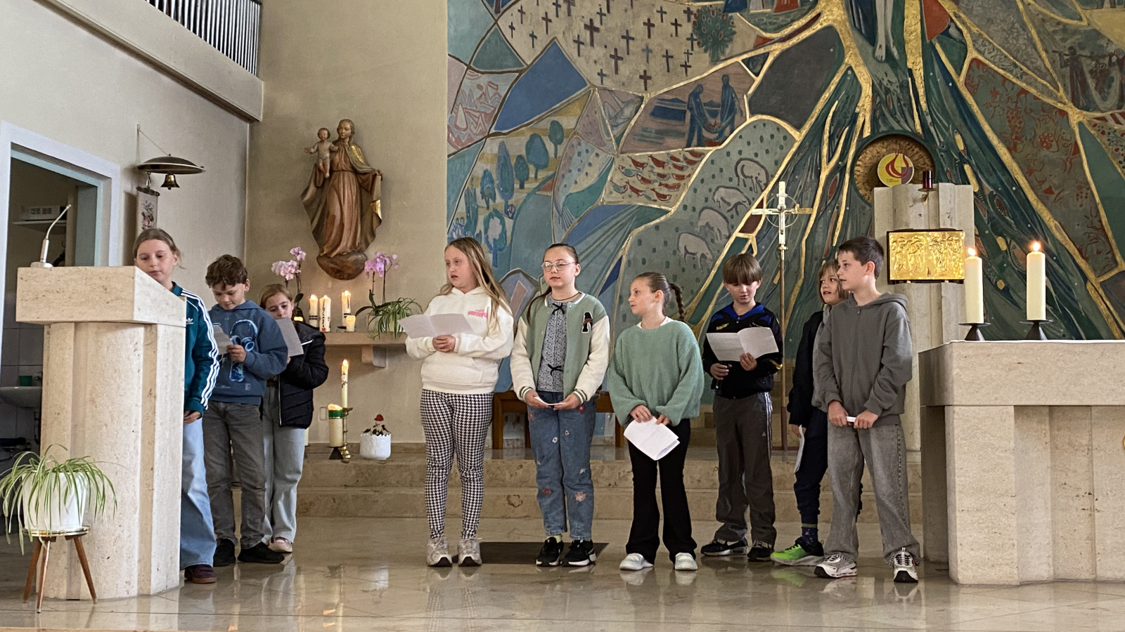 Gruppe von Kindern in der Kirche, die von Blättern lesen, mit Wandgemälde im Hintergrund.