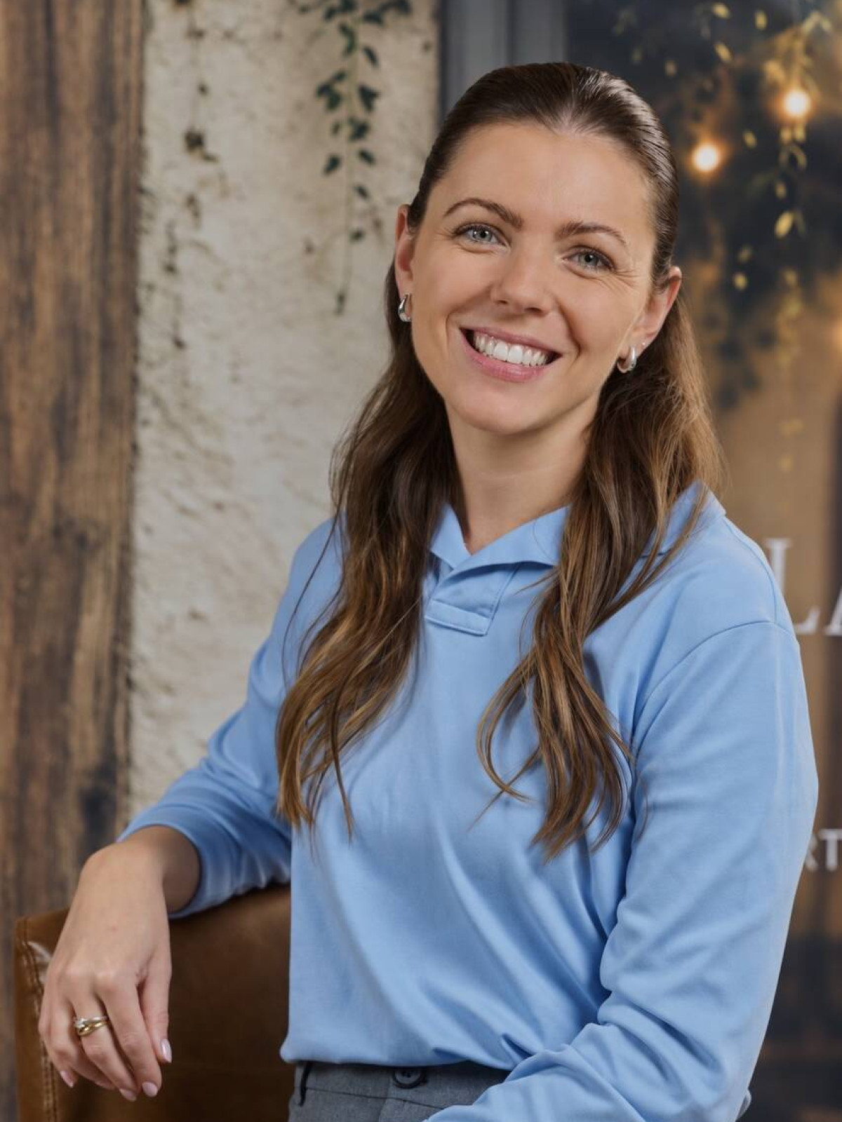 Junge Frau in hellblauer Bluse, sitzt und lächelt.