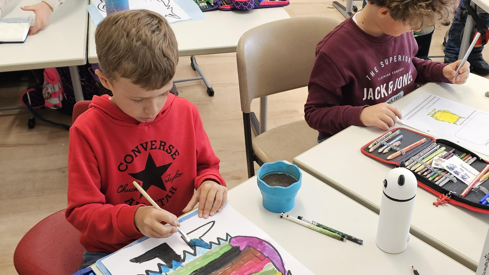 Kinder im Klassenzimmer, die bunte Monsterbilder malen, mit Kunstmaterialien auf den Tischen.