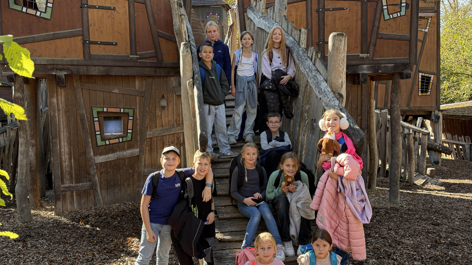 Kindergruppe vor einem großen hölzernen Spielhaus mit dem Schild 'Koboldburg' im Wald.